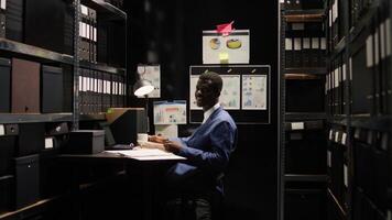 Detective inspector with abilities in criminal investigation, surrounded by case files and evidence, smiles confidently at camera. While having coffee, police officer analyzes clues in archive room. photo