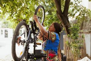 Outdoor detailed shot of african american woman securing and adjusting bike tire rubber for annual maintenance. Healthy female cyclist dismantling damaged bicycle wheel to repair with expert work tool for cycling. photo