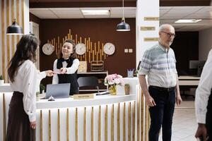 Female receptionist helps an elderly woman at the front desk check in easily and confirms bookings. Retired senior male tourist with luggage is helped by african american porter to his hotel room. photo