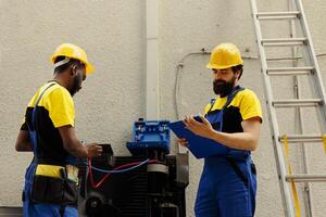 Capable electricians team employed to do air conditioner check, refilling freon. Meticulous wiremen colleagues using manifold indicators to exactly measure the pressure in outside HVAC system photo