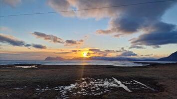 Ocean coastline during golden hour next to snowy mountains and frosty farmlands, icelandic landscapes with wintry weather. Fantastic countryside scenery with hills and open water at sunset. photo