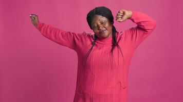 Female fashion influencer yawning in front of camera expressing tiredness after long day. Video capturing african american trendy fashionista with mouth wide-open against pink background. photo