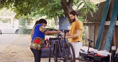 Sports-loving multiethnic couple fastening bike body for examination and maintenance. African american girlfriend assisting boyfriend by clutching modern bicycle to repair-stand in home yard. photo