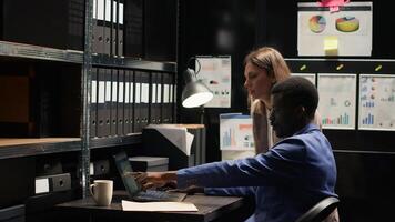 Two private investigators studying forensic evidence on laptop and discussing criminal information in office. Black policeman sips coffee while policewoman shares clues and research for investigation. photo