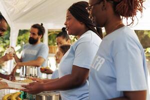 Voluntary multiethnic people distributes needed products and free meals to the hungry, demonstrating charity in aiding the less privileged. Non-profit outdoor food bank serving hot food to the needy. photo