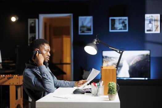 African american man calling investors to obtain new funds for capital investment, working from home to develop business on global market. Young employee chatting on phone call at night. photo