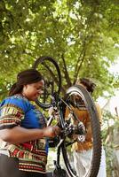 Healthy enthusiastic interracial pair outdoors fixing damaged bicycle components with professional toolkit. Active multiethnic couple using work tool to repair broken bike chain and pedals for summer leisure cycling. photo
