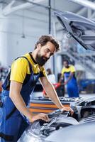 Portrait of car service mechanic examining broken engine using advanced mechanical tools to ensure optimal automotive performance and safety. Happy garage employee conducts annual vehicle checkup photo