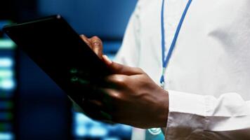 IT programmer using tablet to monitor supercomputer hub security features protecting against unauthorized access, data breaches, phishing attacks and other cybersecurity dangers, close up photo
