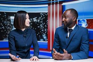 Two reporters broadcasting live information on international television channel, addressing all latest events and giving updates. Diverse presenters creating tv content in studio. photo