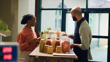 Owner recommends bulk products for woman, presenting variety of chemicals free grains and cooking ingredients stored in reusable jars. Storekeeper explains ecological production process to client. photo