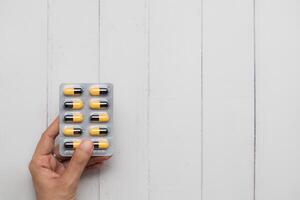 Close up of female hand holding blister pack of pills on white wooden background photo