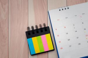 Top view of desk calendar and index sticky note on wooden table background with copy space. photo