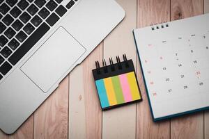 Workspace Organization with Laptop, Index Flags, Calendar on Wooden Desk photo