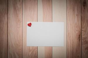 A white paper with a red heart placed on a wooden table photo