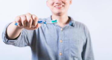 Smiling person showing toothbrush with toothpaste isolated. Unrecognizable man holding brush with toothpaste isolated photo
