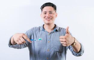 Smiling young man holding a toothbrush gesturing OK. Person holding toothbrush with thumbs up. Guy holding a toothbrush with OK gesture photo