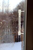 A plastic mercury or alcohol thermometer outside the window of a village house on a frosty day. View from the window into the courtyard, vertical photo