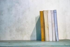 un colección de grueso libros pulcramente arreglado en pie en un mesa en contra un blanco pared antecedentes foto