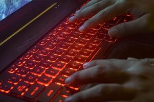 hands typing on a gaming laptop keyboard that glows red photo