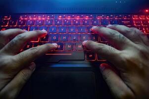 hands typing on a gaming laptop keyboard that glows red photo