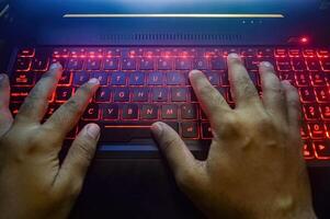 hands typing on a gaming laptop keyboard that glows red photo