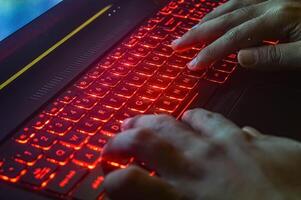 hands typing on a gaming laptop keyboard that glows red photo