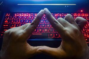 Triangular-shaped fingers against the background of a gaming laptop keyboard equipped with backlight photo