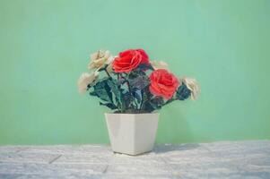 A decorative plastic fake flower bouquet in a white flower vase against a turquoise green wall background photo