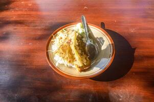 a plate of East Javanese Madiun pecel rice on a wooden table in the morning sunlight photo