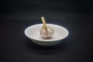 a garlic on a plain white plate isolated on a plain black background photo