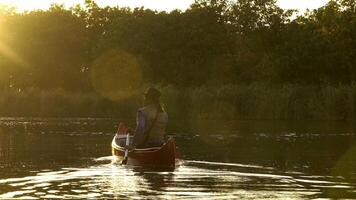 un' cowboy nel un' rosso canoa galleggia su il fiume nel il foresta. bellissimo luce del sole a tramonto. storico ricostruzione di vita nel il selvaggio ovest di America. 4k video