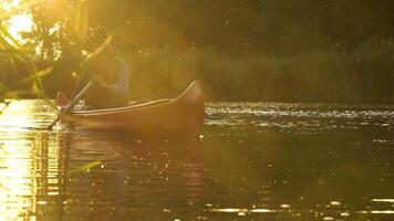 un' cowboy nel un' rosso canoa galleggia su il fiume nel il foresta. bellissimo luce del sole a tramonto. storico ricostruzione di vita nel il selvaggio ovest di America. 4k video