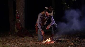 cowboy vicino il fuoco nel il foresta a notte. storico ricostruzione di vita nel il selvaggio ovest di America. 4k video
