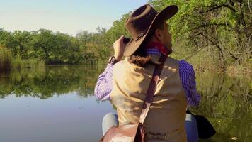 portret van een cowboy zwemmen in een kano Aan de rivier- in de Woud. historisch wederopbouw van leven in de wild west van Amerika. 4k video