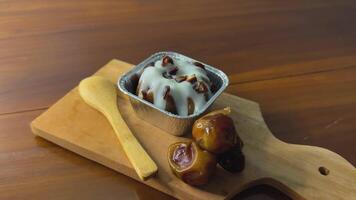 Appetizer with date pudding and some chopped dates topped with vanilla sauce on a wooden cutting board Concept of indulgence and comfort video