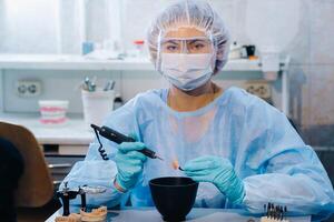 un dental técnico en protector ropa es trabajando en un protésico diente en su laboratorio foto