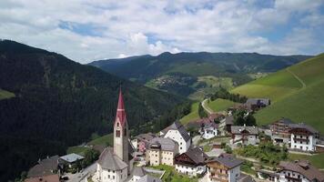 Aerial flight over the bell tower of a church in a small alpine village in the Dolomites. European Alps, Tyrol 4K video