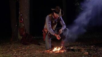 Cowboy in der Nähe von das Feuer im das Wald beim Nacht. historisch Wiederaufbau von Leben im das wild Westen von Amerika. 4k video