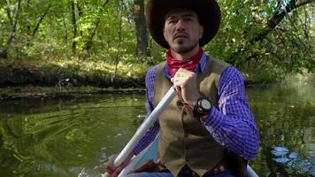 A cowboy in a canoe floats on the river in the forest. Historical reconstruction of life in the wild west of America. 4K video