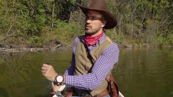 Portrait of a cowboy swimming in a canoe on the river in the forest. Historical reconstruction of life in the wild west of America. 4K video