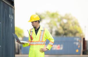 Workers in the import and export industry holding a laptop and standing on the front of container to inspect the container's cargo. photo