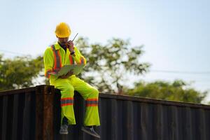 Workers in the import and export industry holding a laptop and sitting on a shipping container to inspect the container's cargo. photo