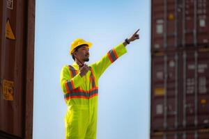 A male worker stands on a container box while wearing a safety suit. Use the walkie-talkie to communicate with coworkers on the floor below the container. photo