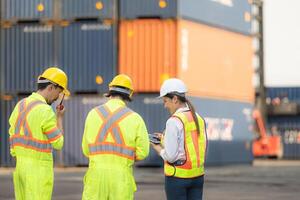 Group of workers in the import and export industry use walkie talkies to communicate with drivers of reach stacker containers in an empty container warehouse. photo