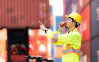 Portrait of a warehouse worker speaking on a walkie talkie with a coworker in an empty container warehouse while driving a scooter to inspect work photo