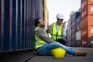 A guy worker was involved in a leg accident in a container storage yard. A colleague was using the walkie talkie to request immediate aid. photo