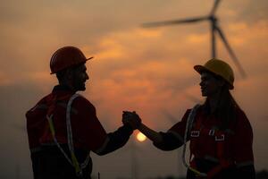 ingenieros sacudir manos en un viento turbina granja con puesta de sol antecedentes a el final de el día. foto