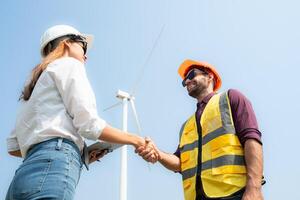 Engineer and technician shaking hands with wind turbine on the background of blue sky photo