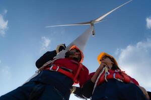 Low angle view of engineers standing in front of a wind turbine, Using the walkie talkie to communicate with co-workers photo